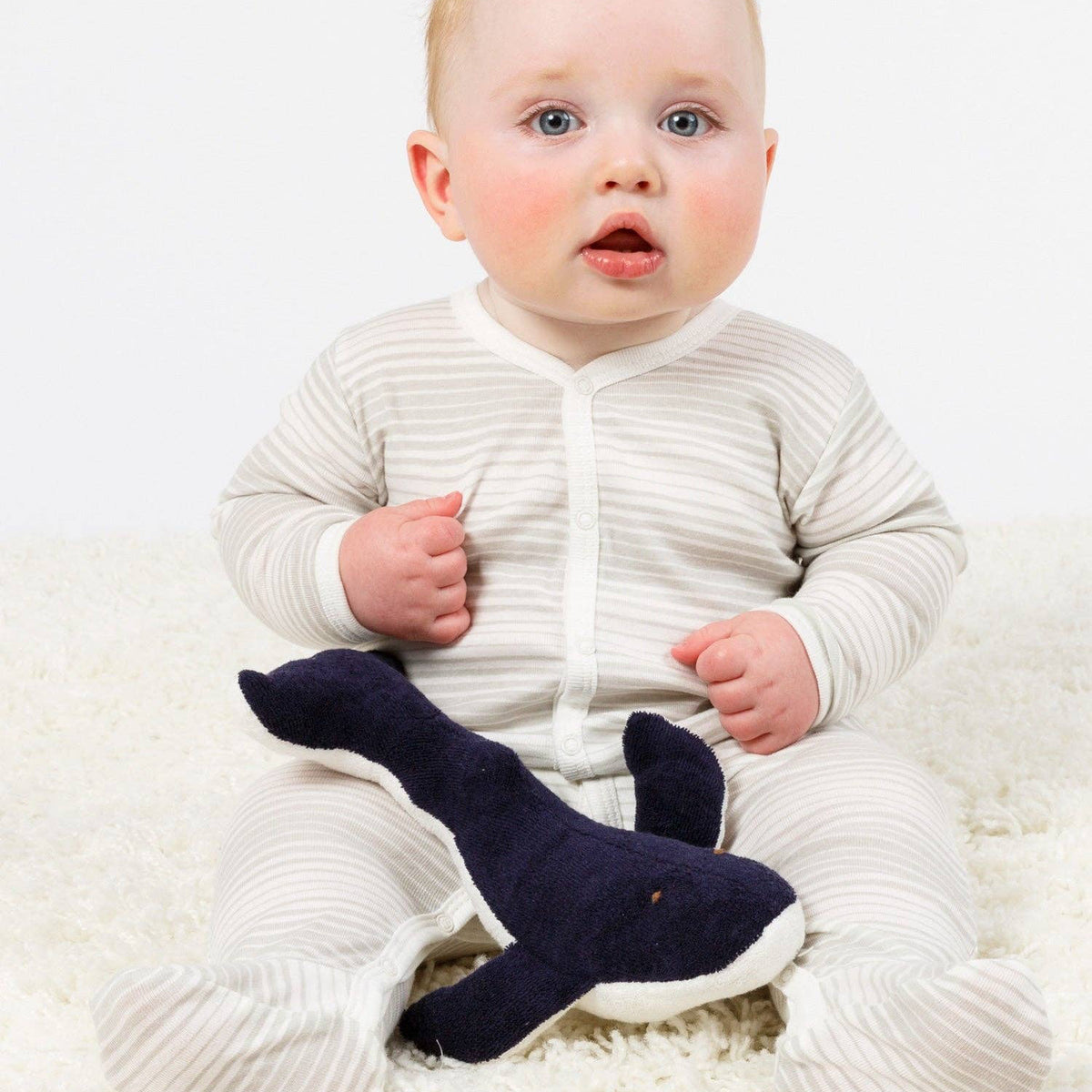 Baby wearing a white outfit with navy socks on a white background