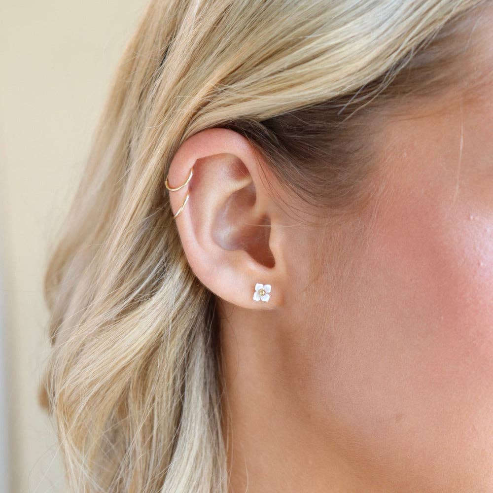 Close-up of a person wearing a gold hoop earring and a diamond stud earring.