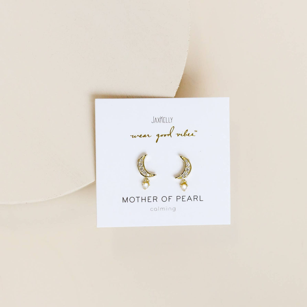 Gold earrings on a white card with 'Jamelie' branding on a beige background