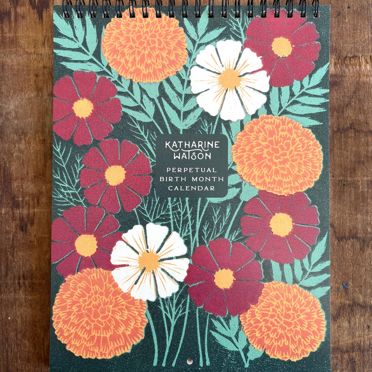 Floral design calendar by Katharine Watson on a wooden surface