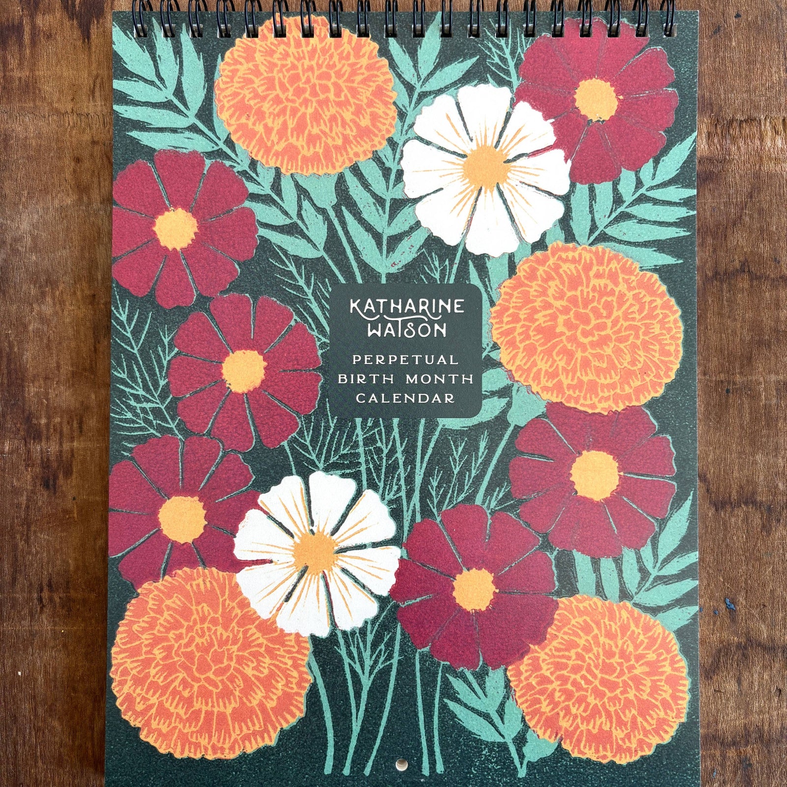 Floral design calendar by Katharine Watson on a wooden surface