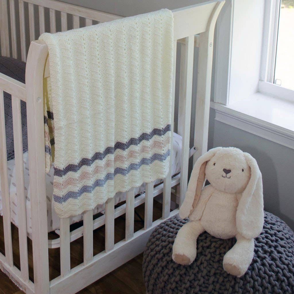 White crib with a textured blanket and a plush bunny toy on a cushion in a nursery.