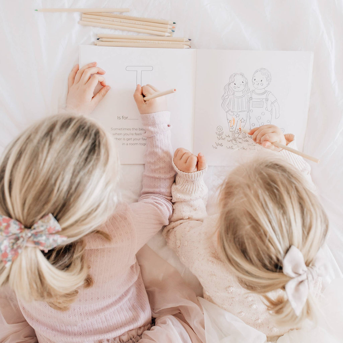 Two children sitting together, drawing on paper with pencils.