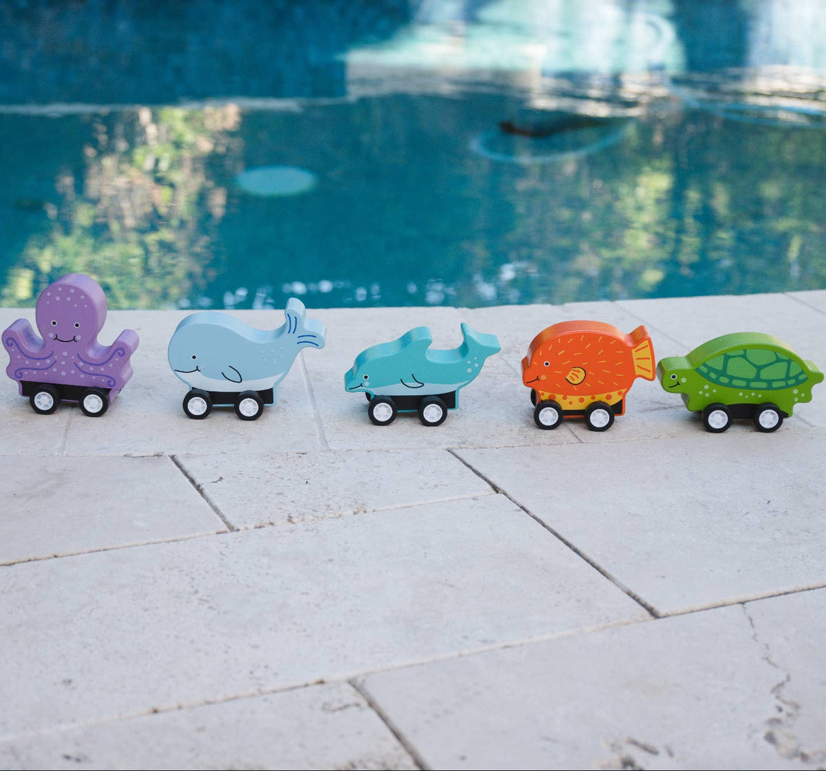 Colorful toy cars on a stone surface with a pool in the background