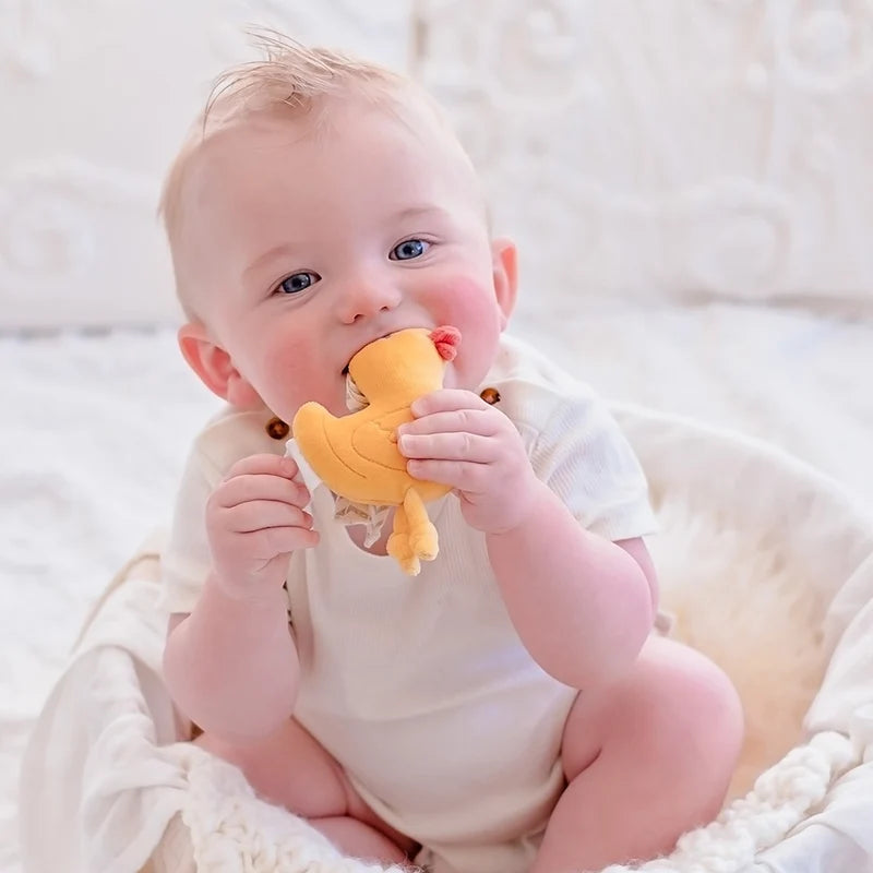 Baby holding a yellow teething toy in a white crib
