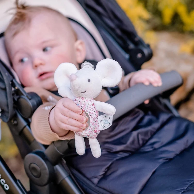 Baby in a stroller holding a plush toy, with a blurred natural background