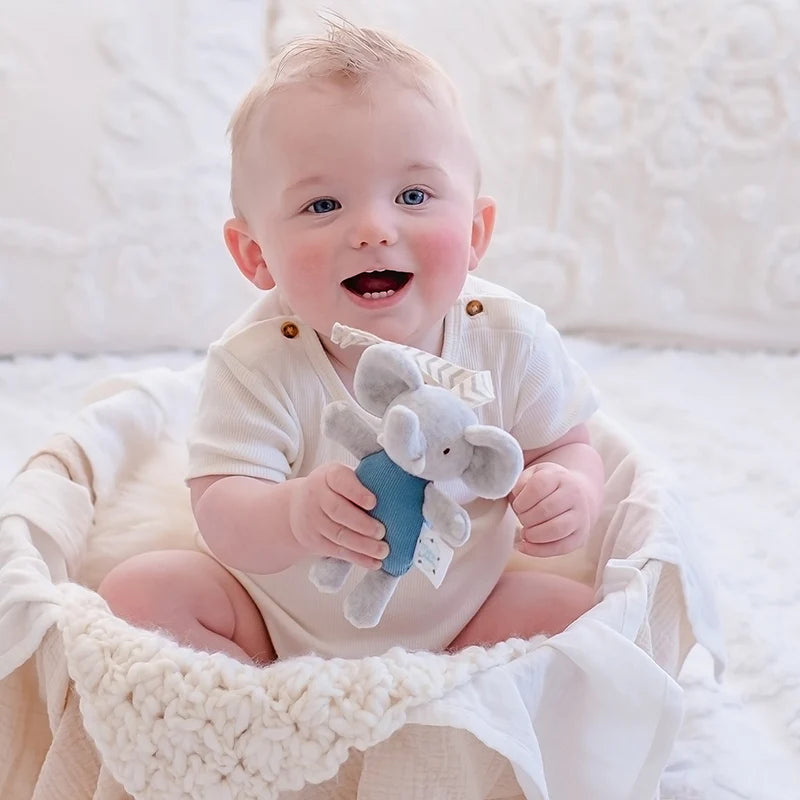 Baby holding a toy elephant in a white textured blanket