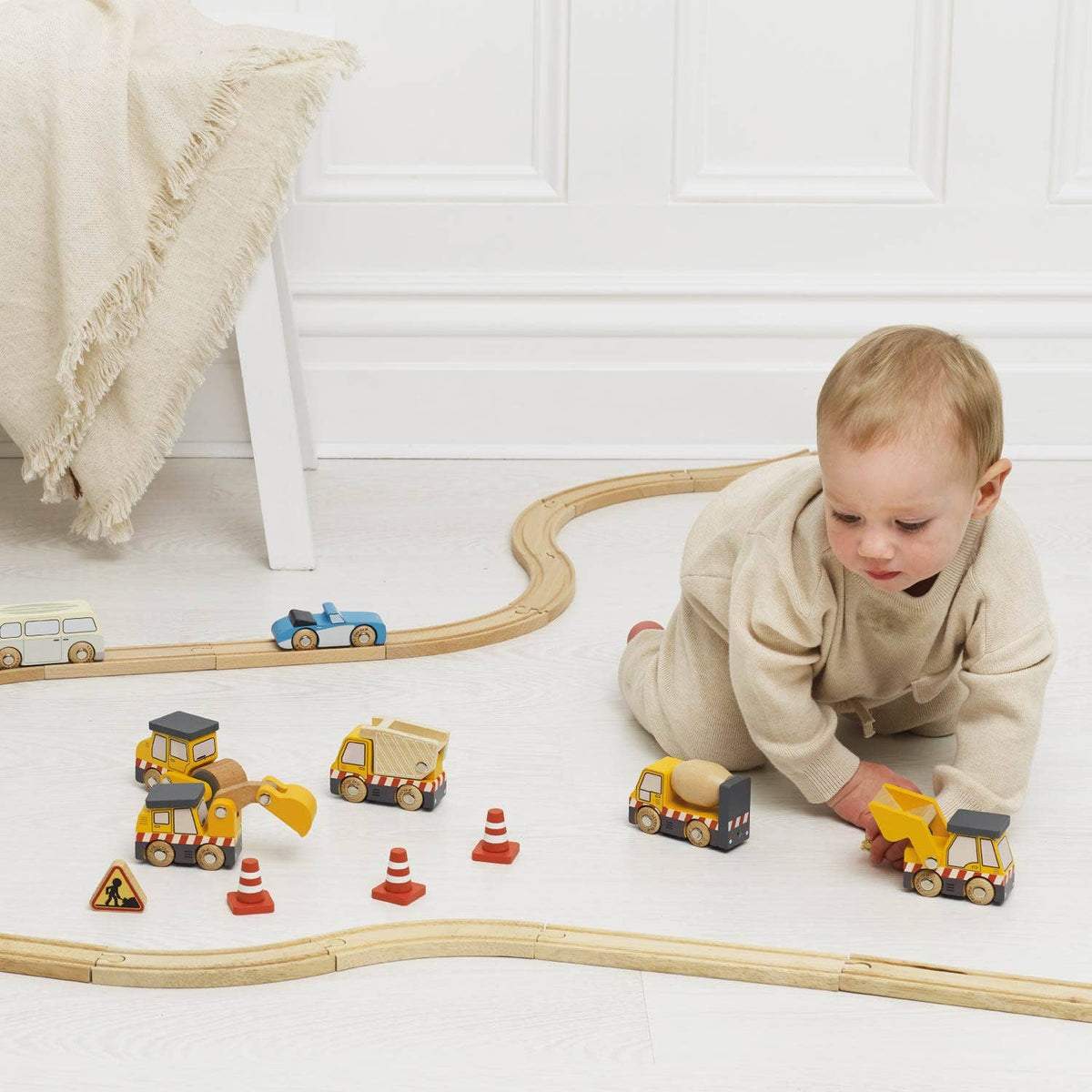 Child playing with toy cars and train tracks on a white floor.