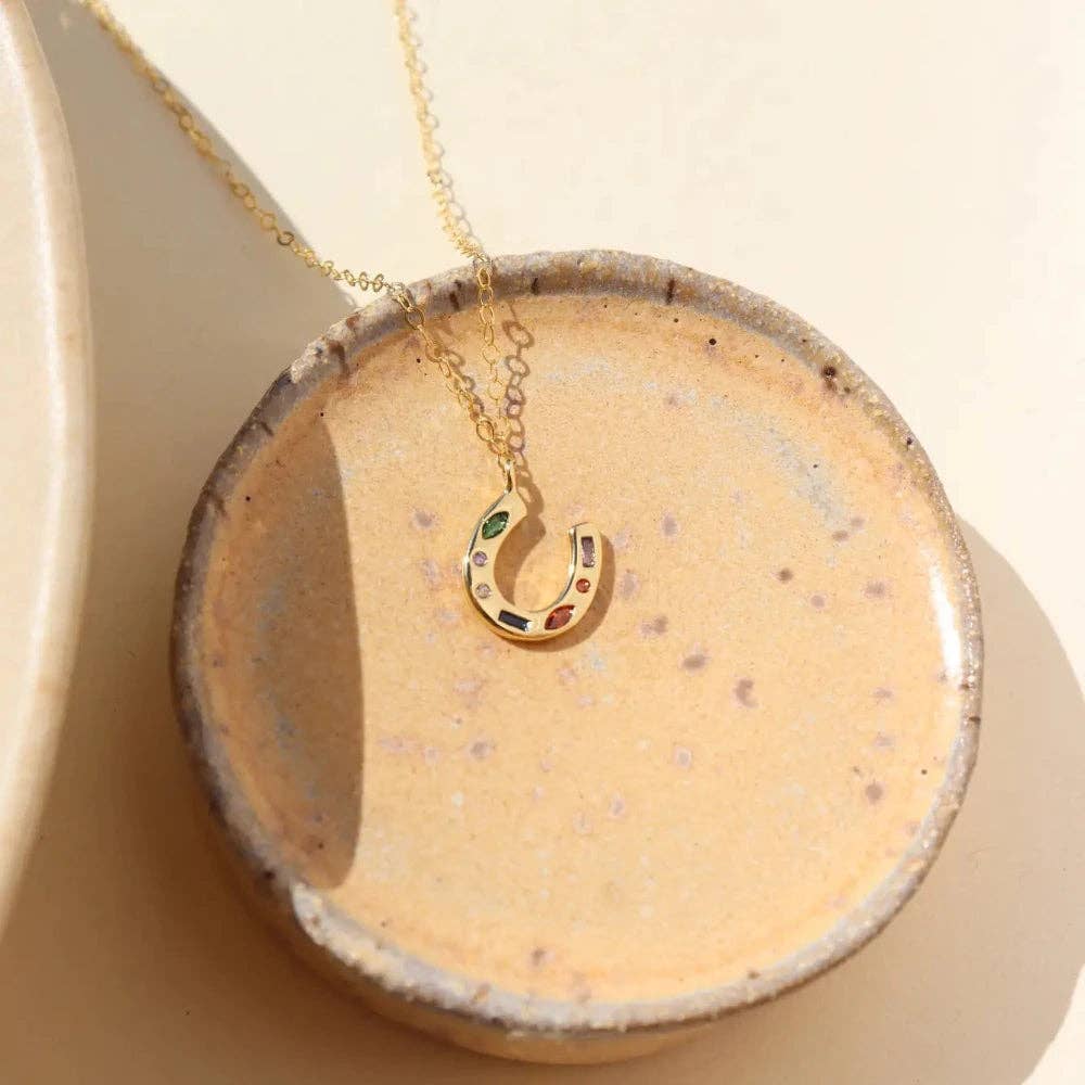 Gold necklace with a horseshoe pendant on a beige dish