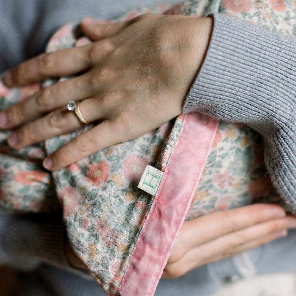 Person holding a baby wrapped in a floral blanket with a pink edge.