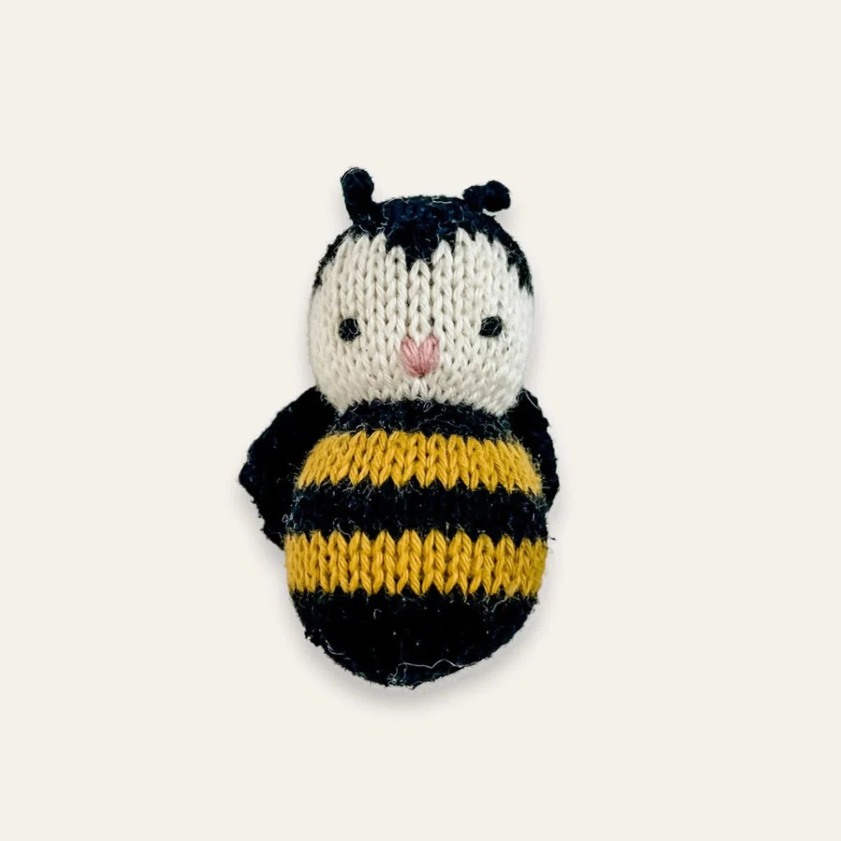 A knitted bumblebee plush toy  featuring a black and yellow striped body, a white face, and small black antennae, centered on a light cream background.