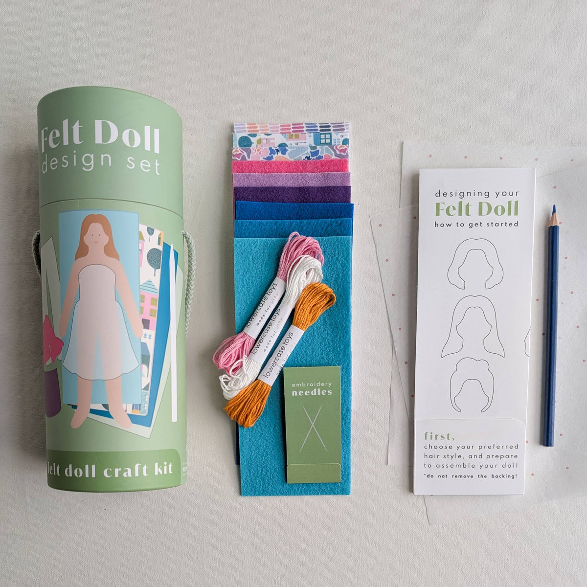 Felt doll design set with cylindrical container, fabric strips, needles, and instructions on a light gray background.
