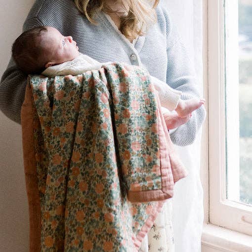 Woman holding a baby wrapped in a floral blanket by a window