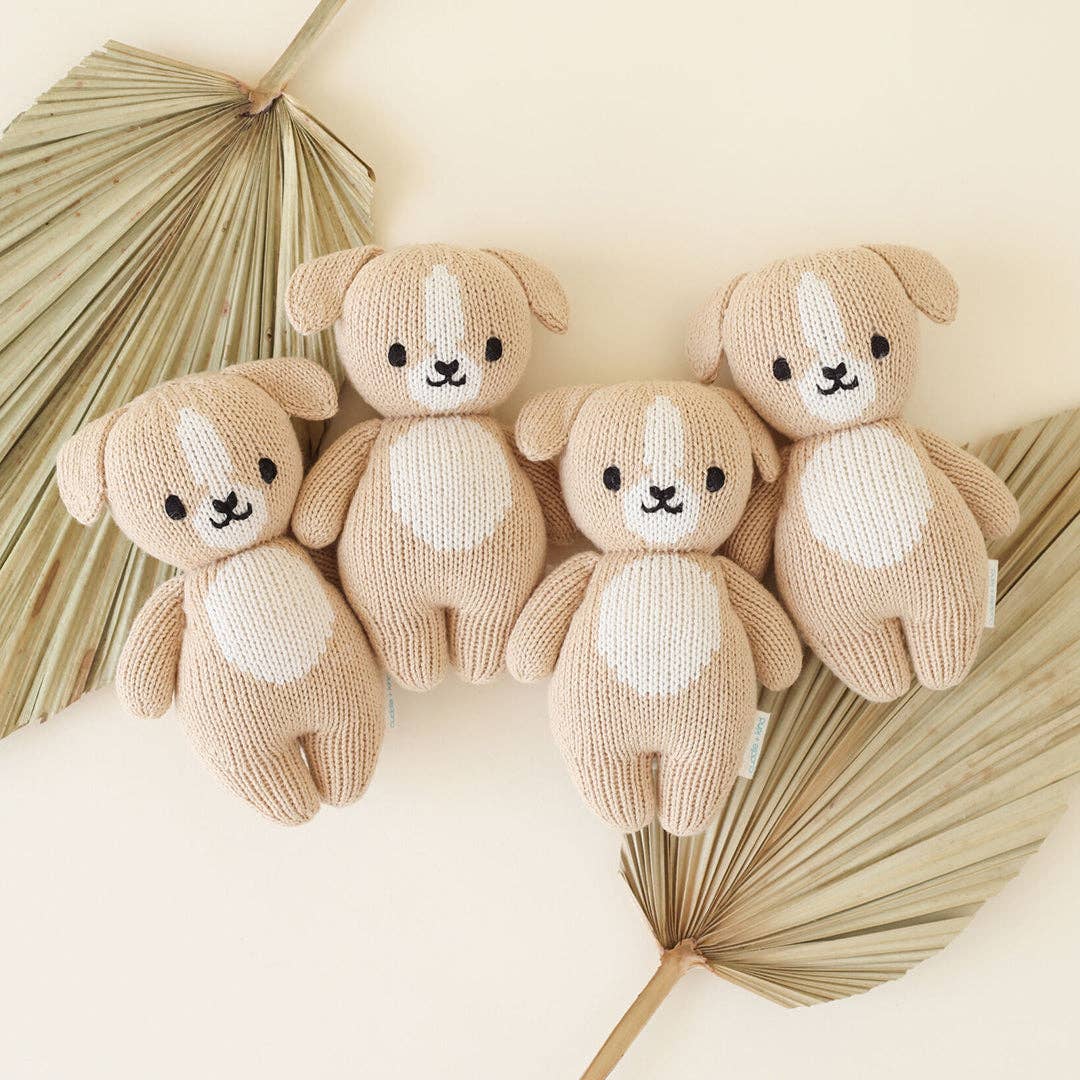 Four knitted dogs with white patches on a neutral background