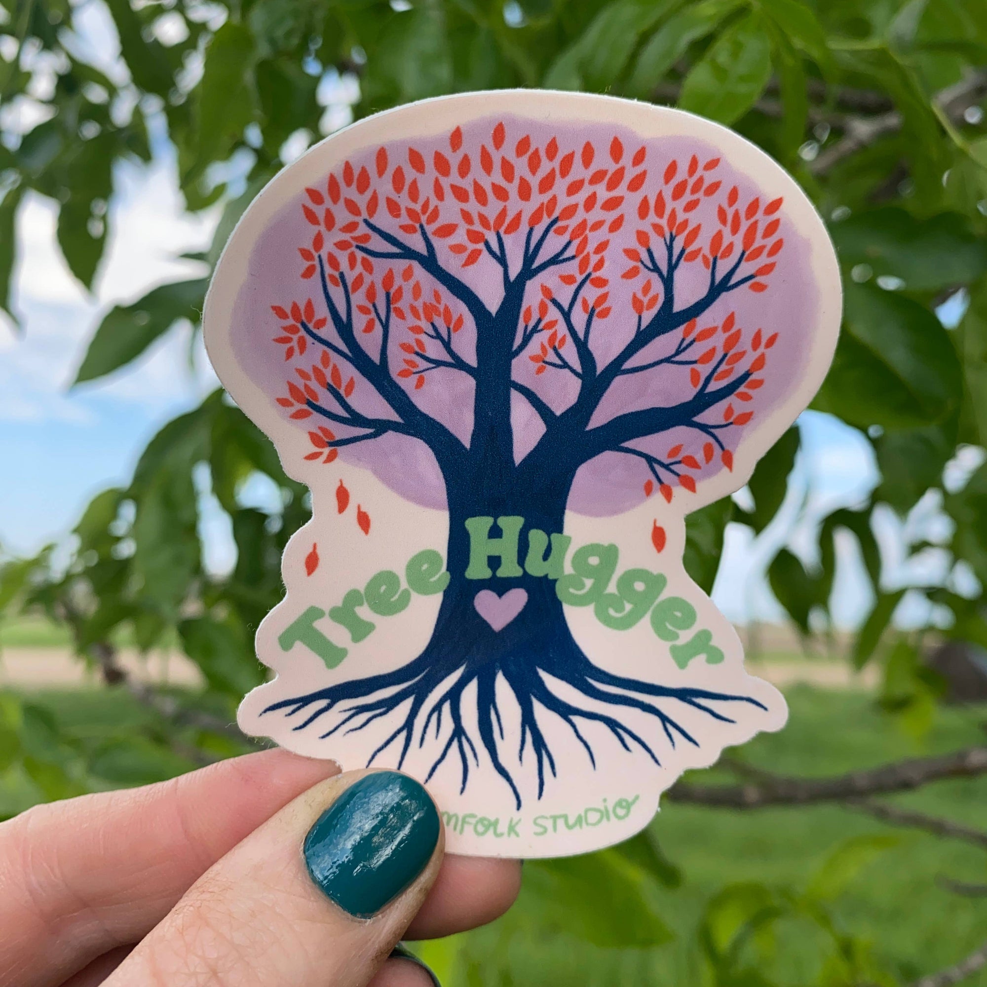 Sticker with tree design and 'Tree Hugger' text held in front of a tree