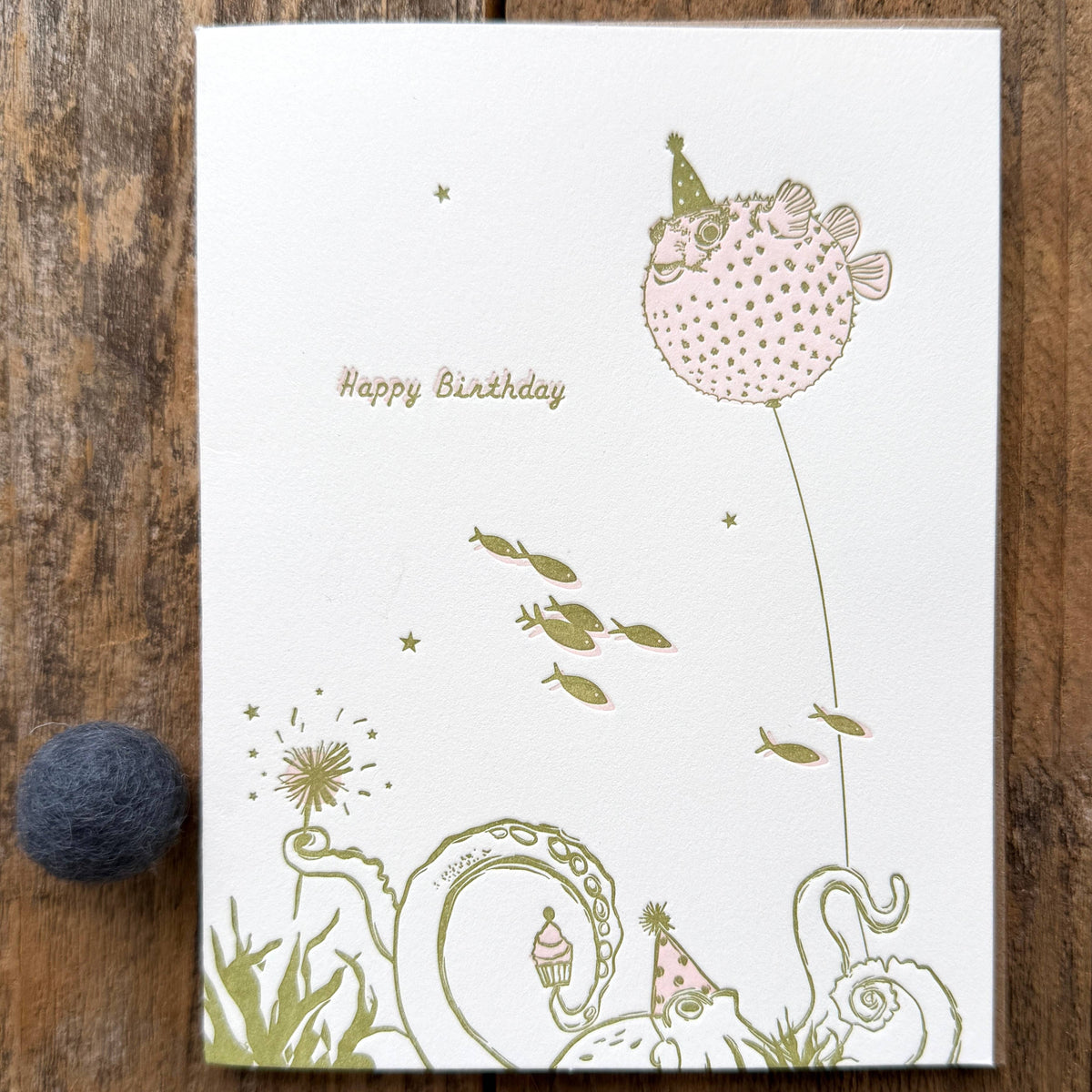 Birthday card with a fish balloon and party hats on a wooden surface