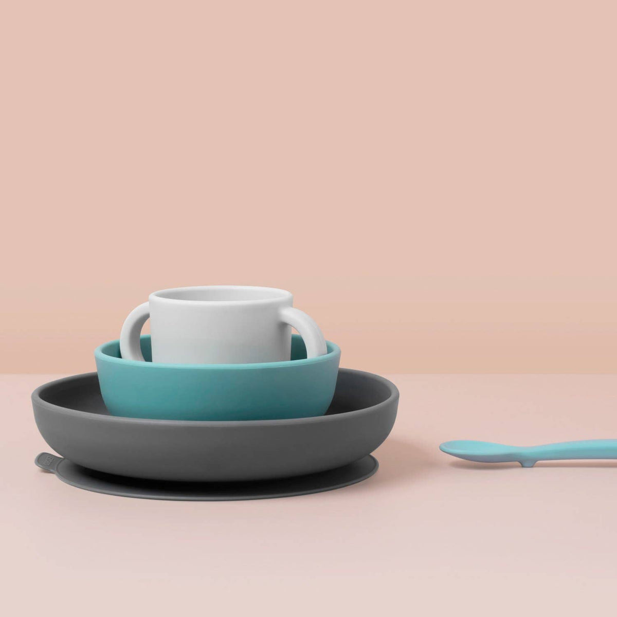 Set of silicone dishes including a mug, bowl, and plate on a beige background