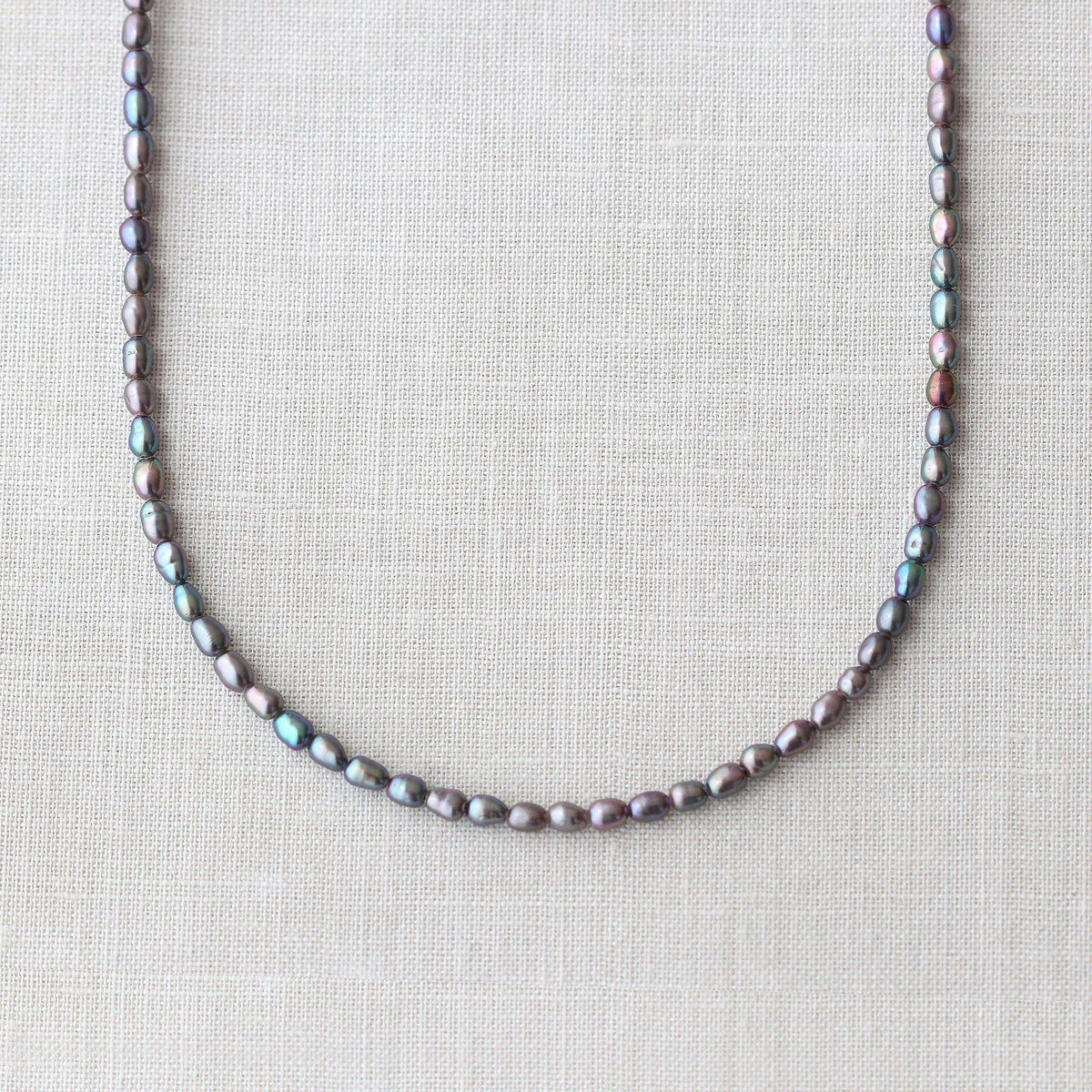 A strand of freshwater pearls draped in a U-shape on a textured beige linen fabric background.