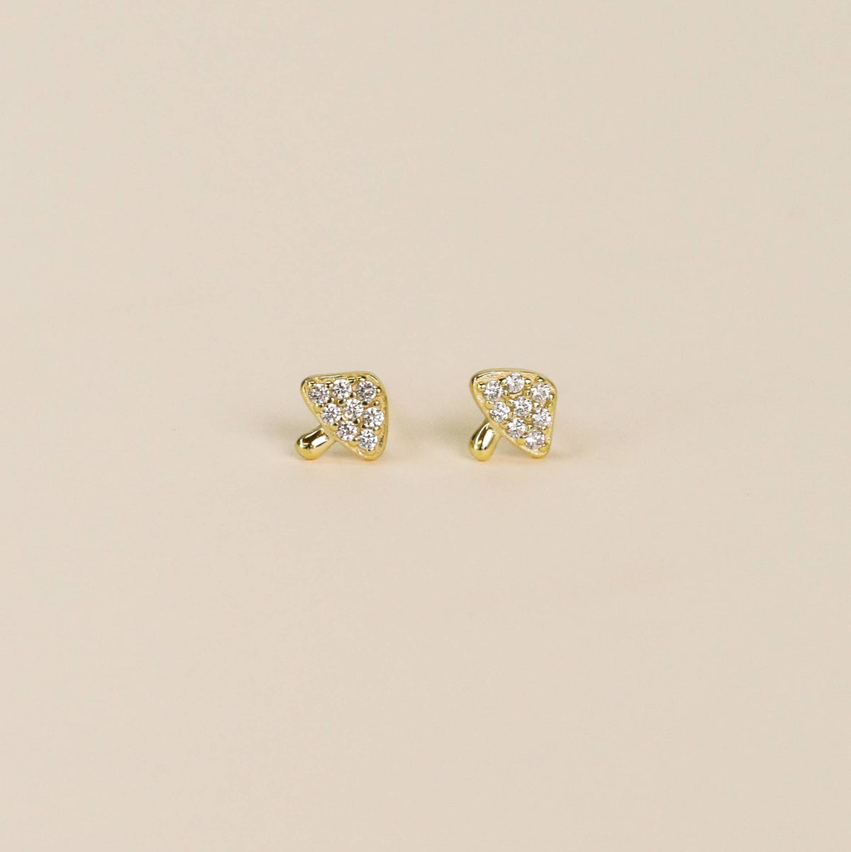 Gold earrings with clear gemstones on a beige background