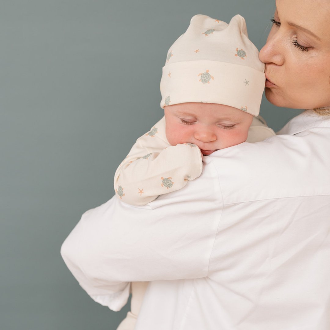 Woman holding a baby wrapped in a white blanket against a gray background