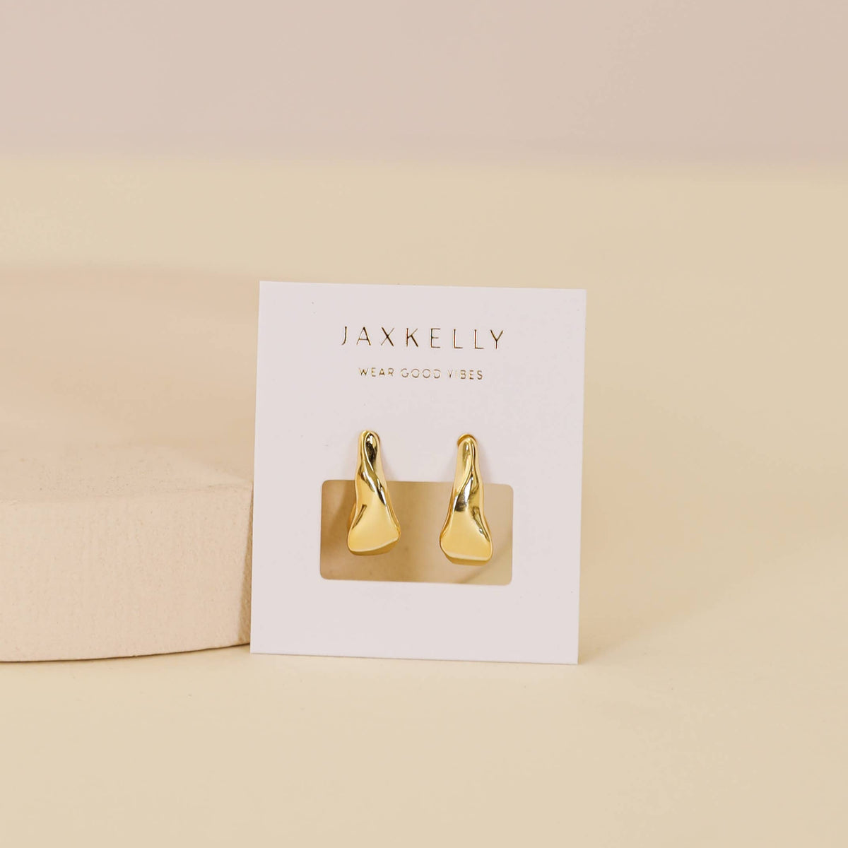 Gold earrings on a Jaxkelly branded card against a beige background