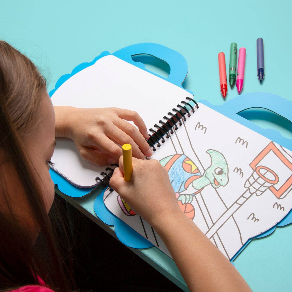 Child coloring a dino with crayons on a blue table