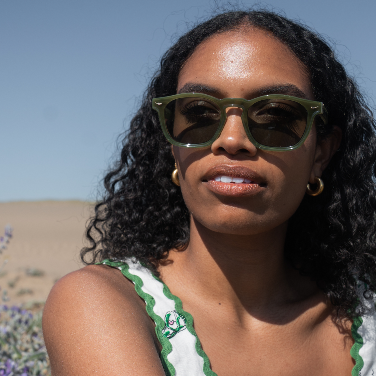 Woman wearing green sunglasses with a clear blue sky background