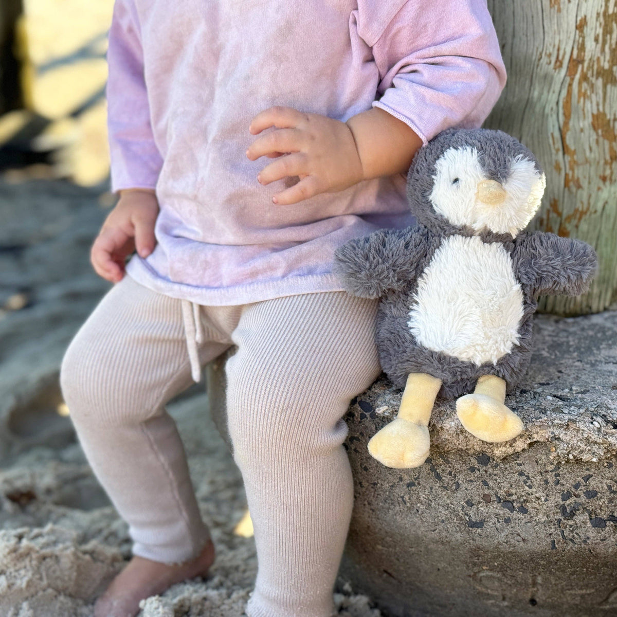 Child holding a plush penguin toy on a sandy surface