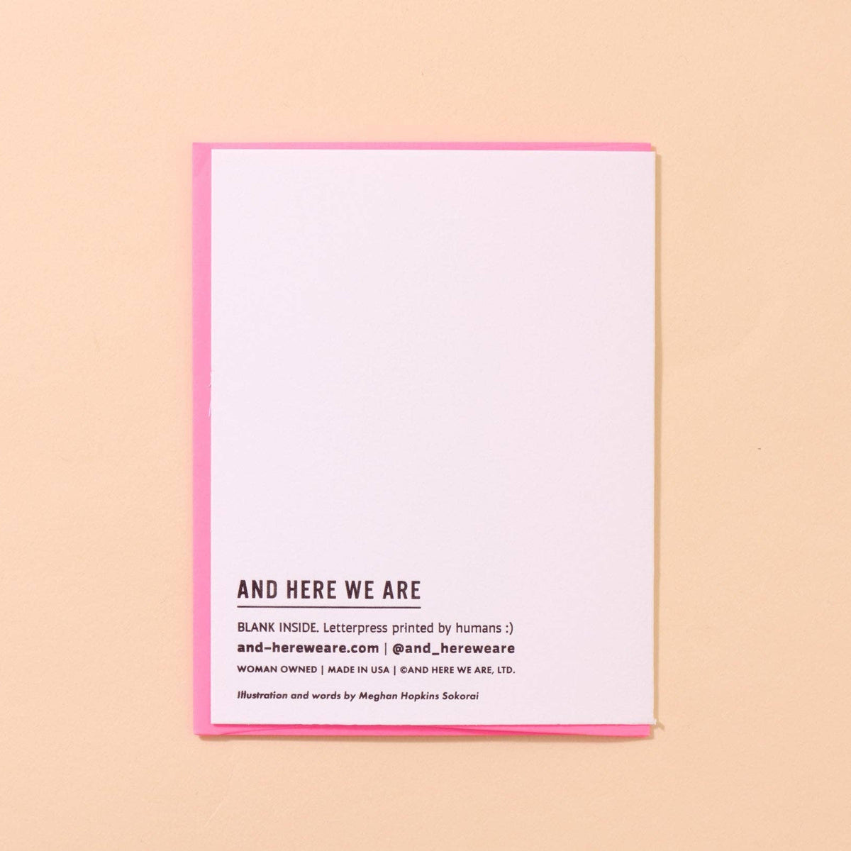 A minimalist art print or postcard with a white center and a pink border, featuring the text 'AND HERE WE ARE' in black. It is photographed flat on a solid peach-colored background.