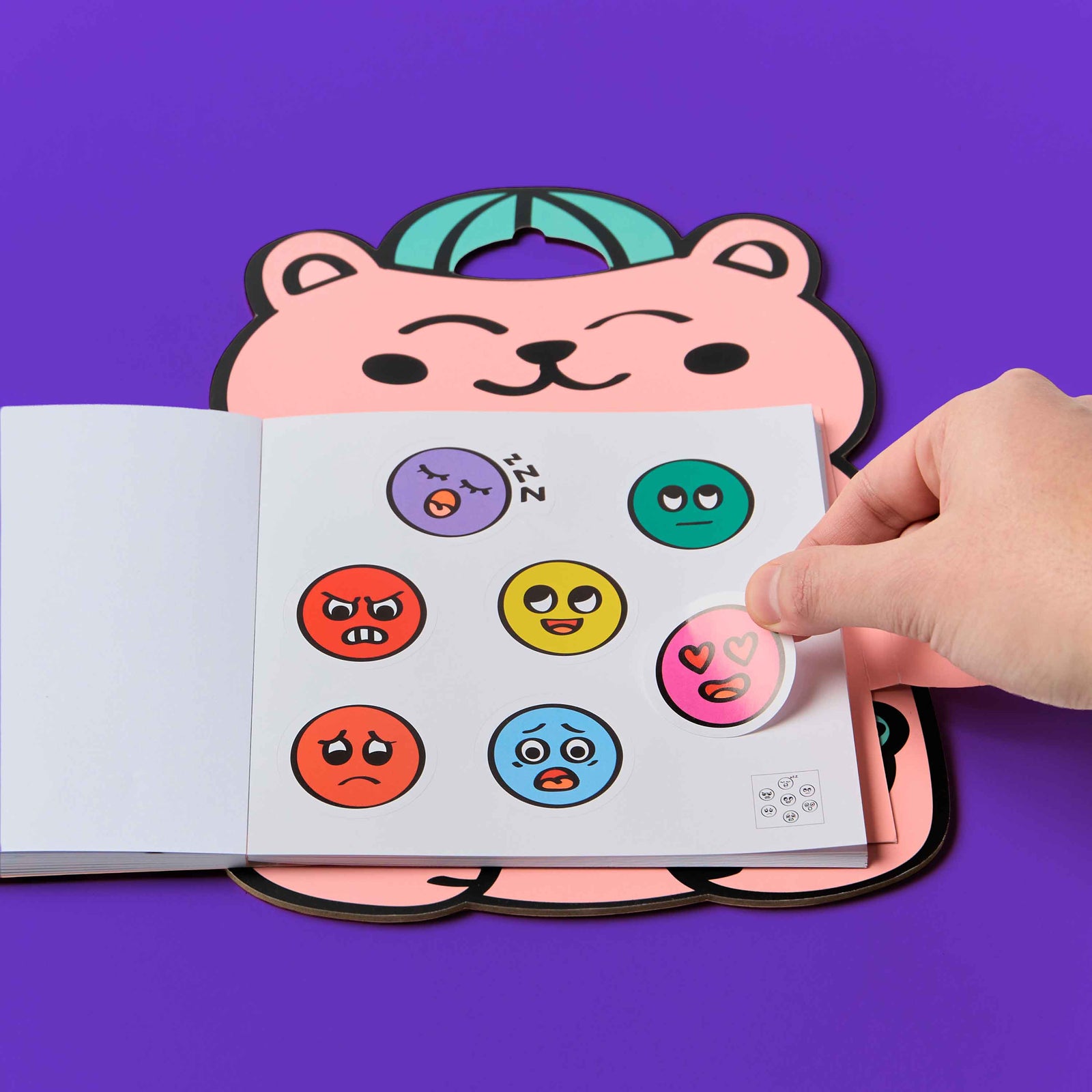 Cartoon bear holding a Montessori stickers book against a purple background