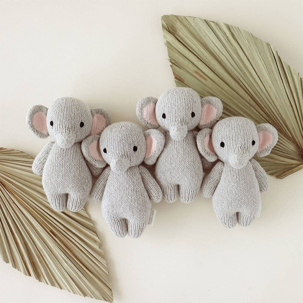 Four knitted elephant toys on a light background with decorative leaves.