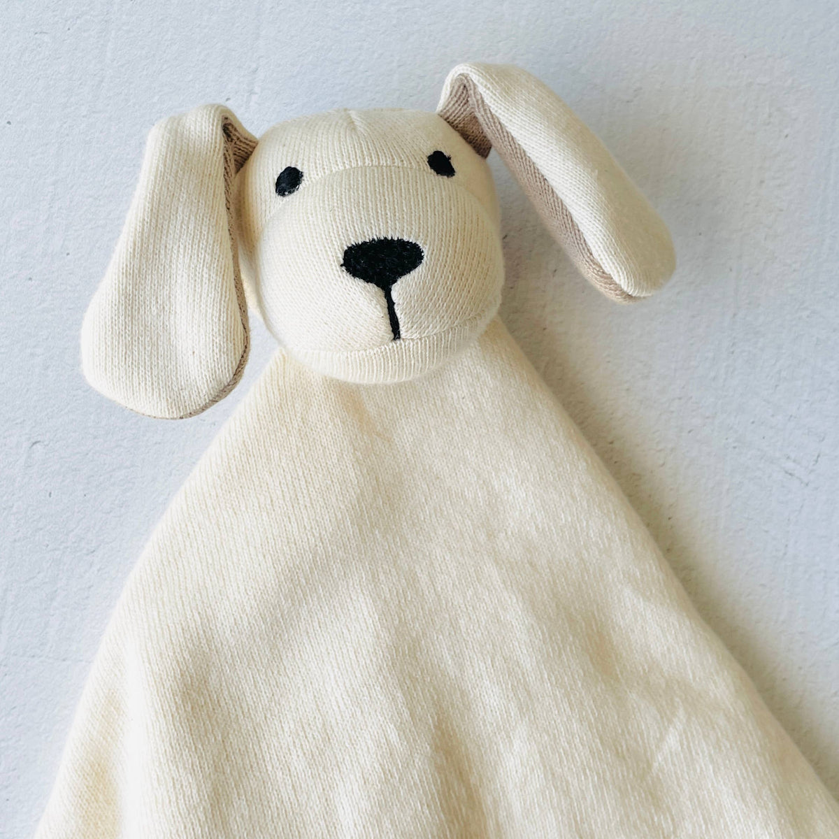 Cream-colored dog-shaped comfort blanket on a light gray background