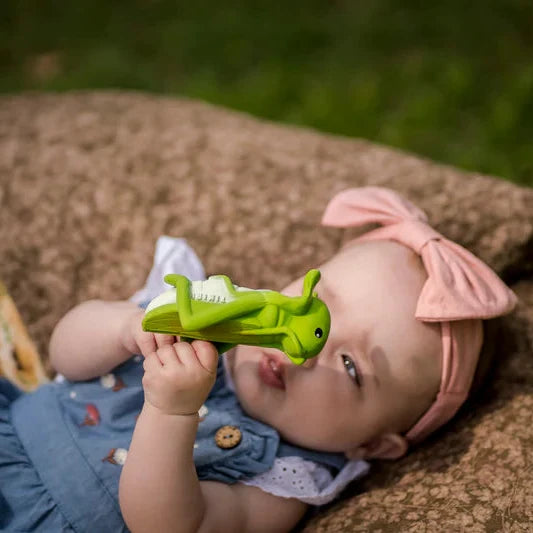 Baby lying on a blanket holding a green toy, wearing a pink headband.