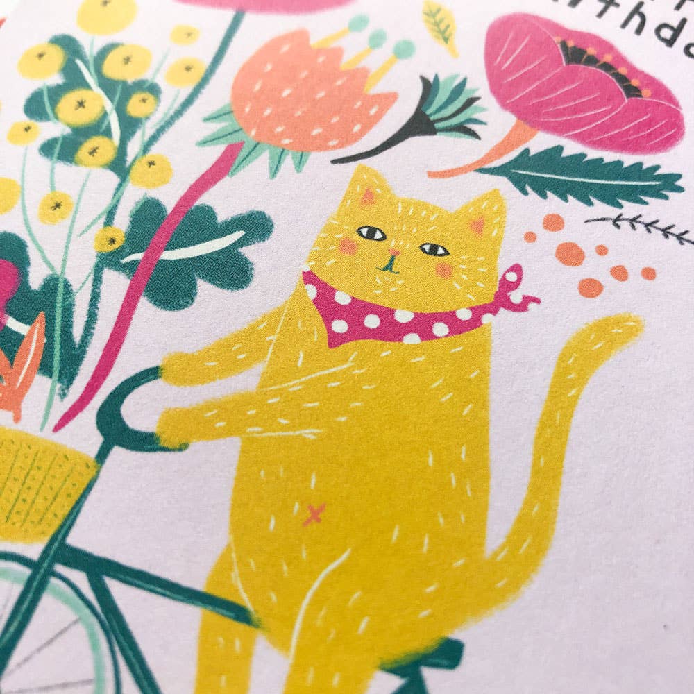 Birthday card with a cat riding a bike and flowers, on a white background