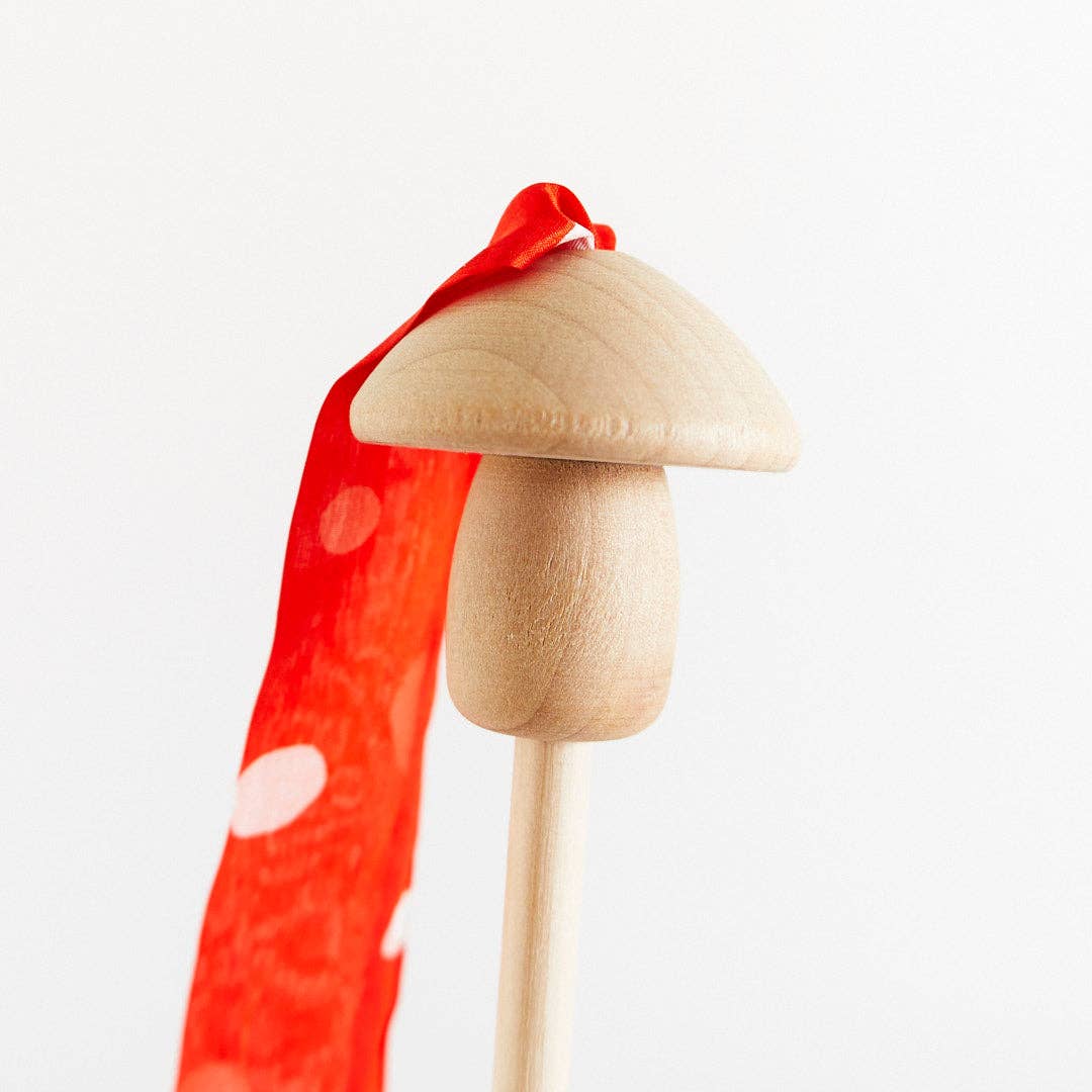 Wooden toy mushroom with a red silk streamer on a white background