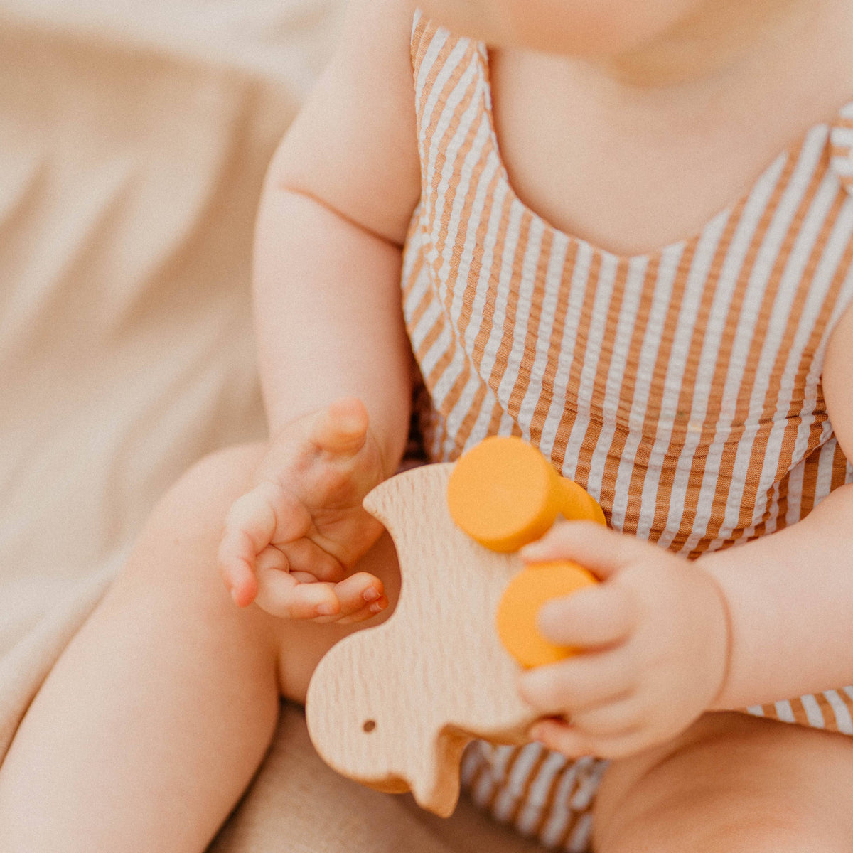 Baby holding a wooden toy with a yellow top on a soft surface