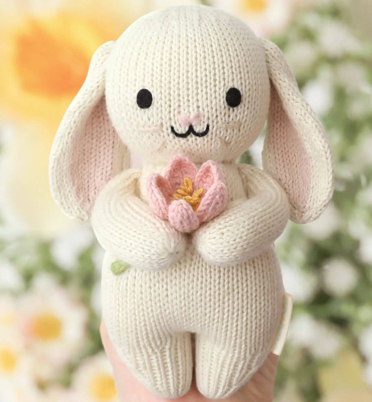 Knitted bunny holding a pink flower with a blurred floral background