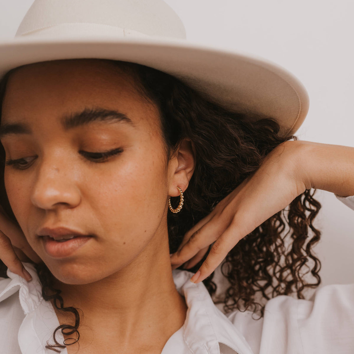 Woman wearing a beige hat and white shirt against a plain background