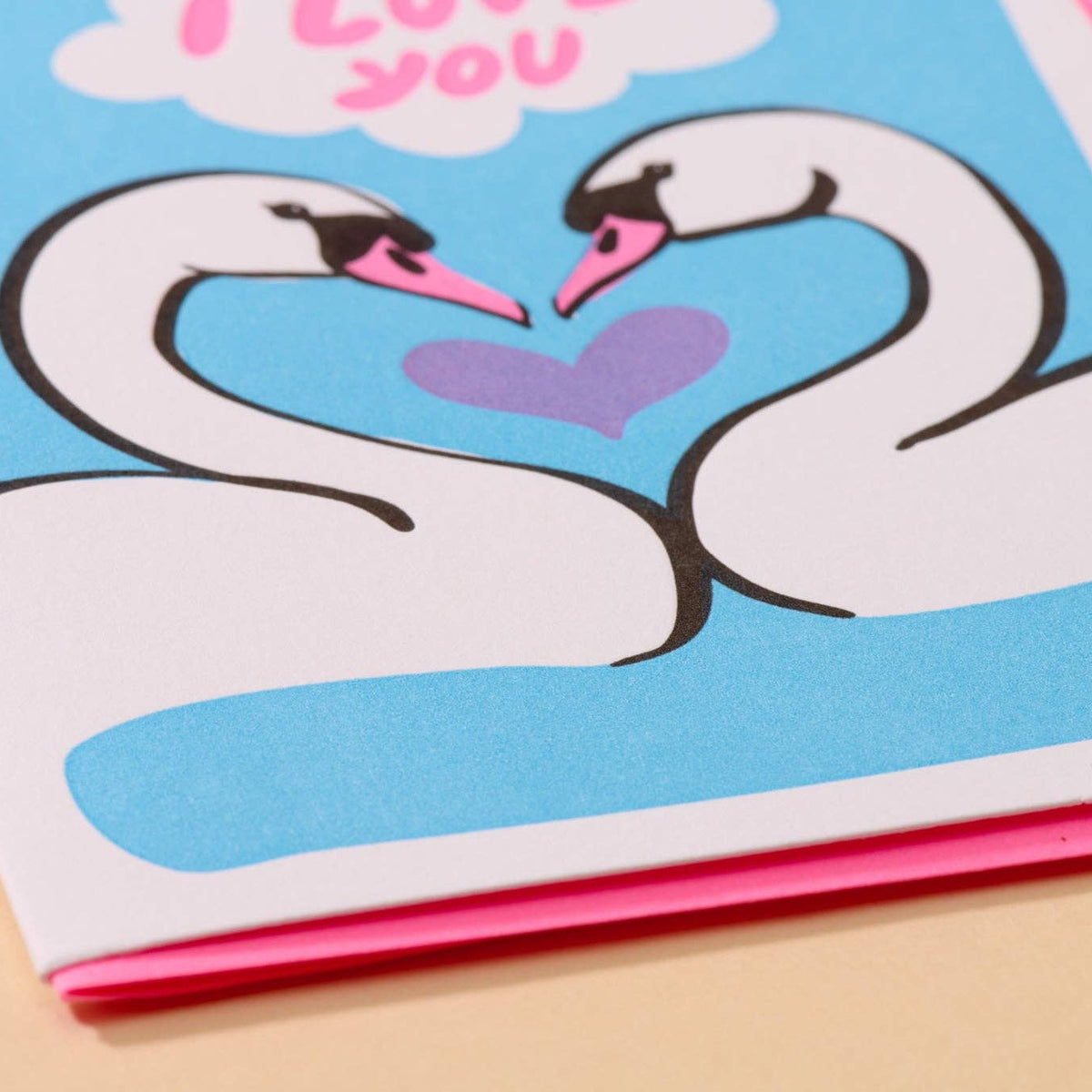 Card with two swans forming a heart shape and 'I love you' text on a blue background.