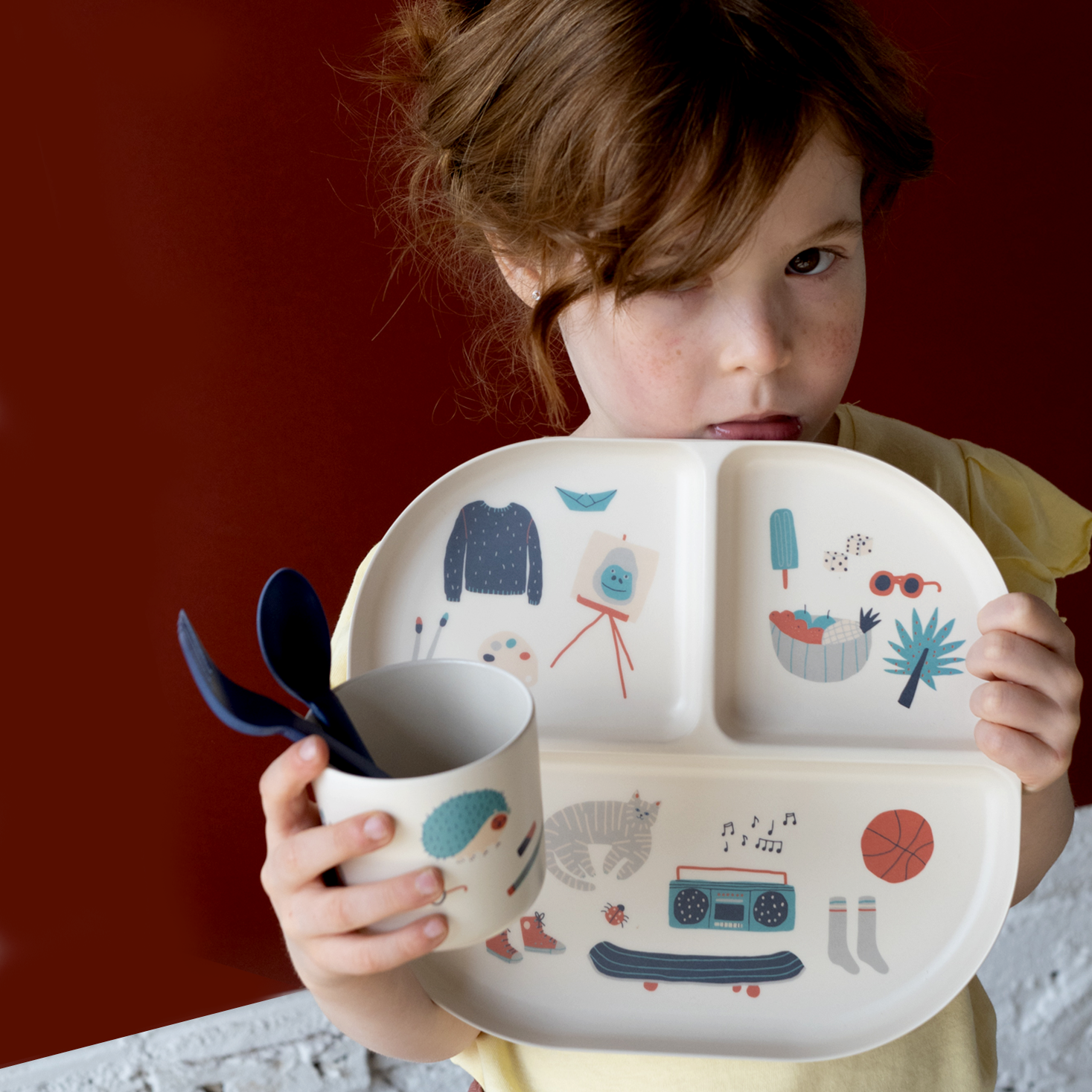 Child holding a children's plate with cartoon designs against a red background