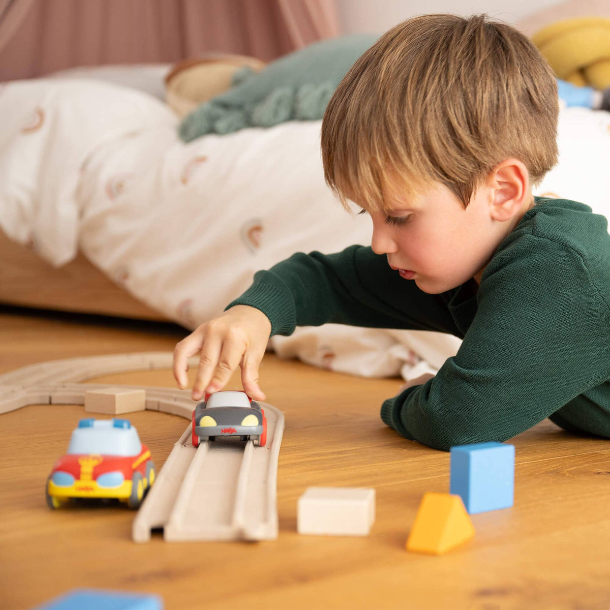 Child playing with toy cars and tracks on a wooden floor