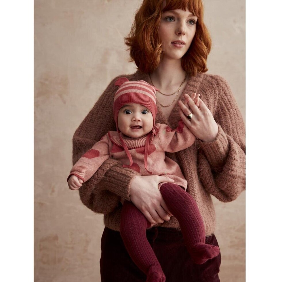 Woman holding a baby wearing matching pink outfits against a beige background