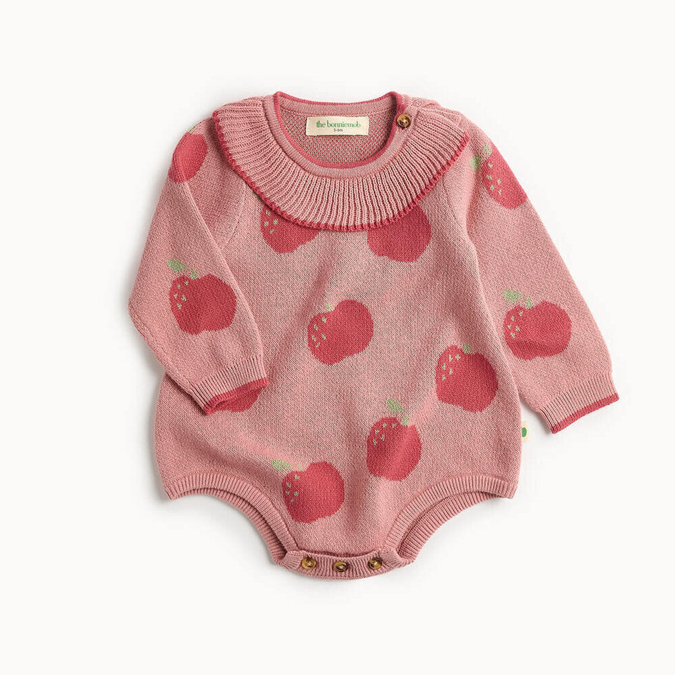 Pink knitted baby romper with apple pattern on a white background