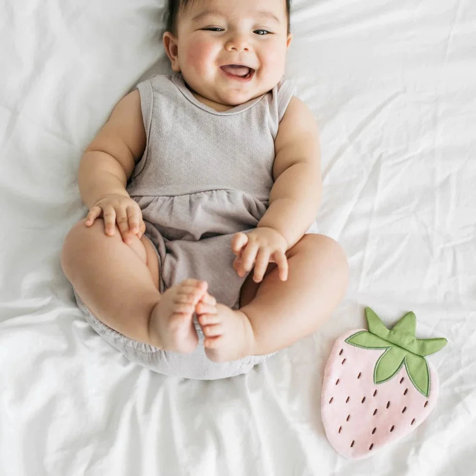 Baby sitting on a white blanket with a pink strawberry toy