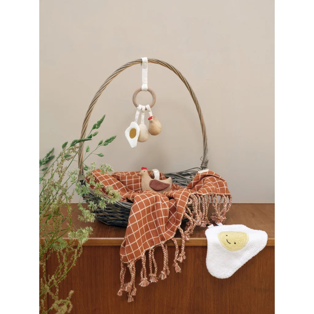 Baby crib with brown blanket, white rattle, and hanging toy on a wooden surface.