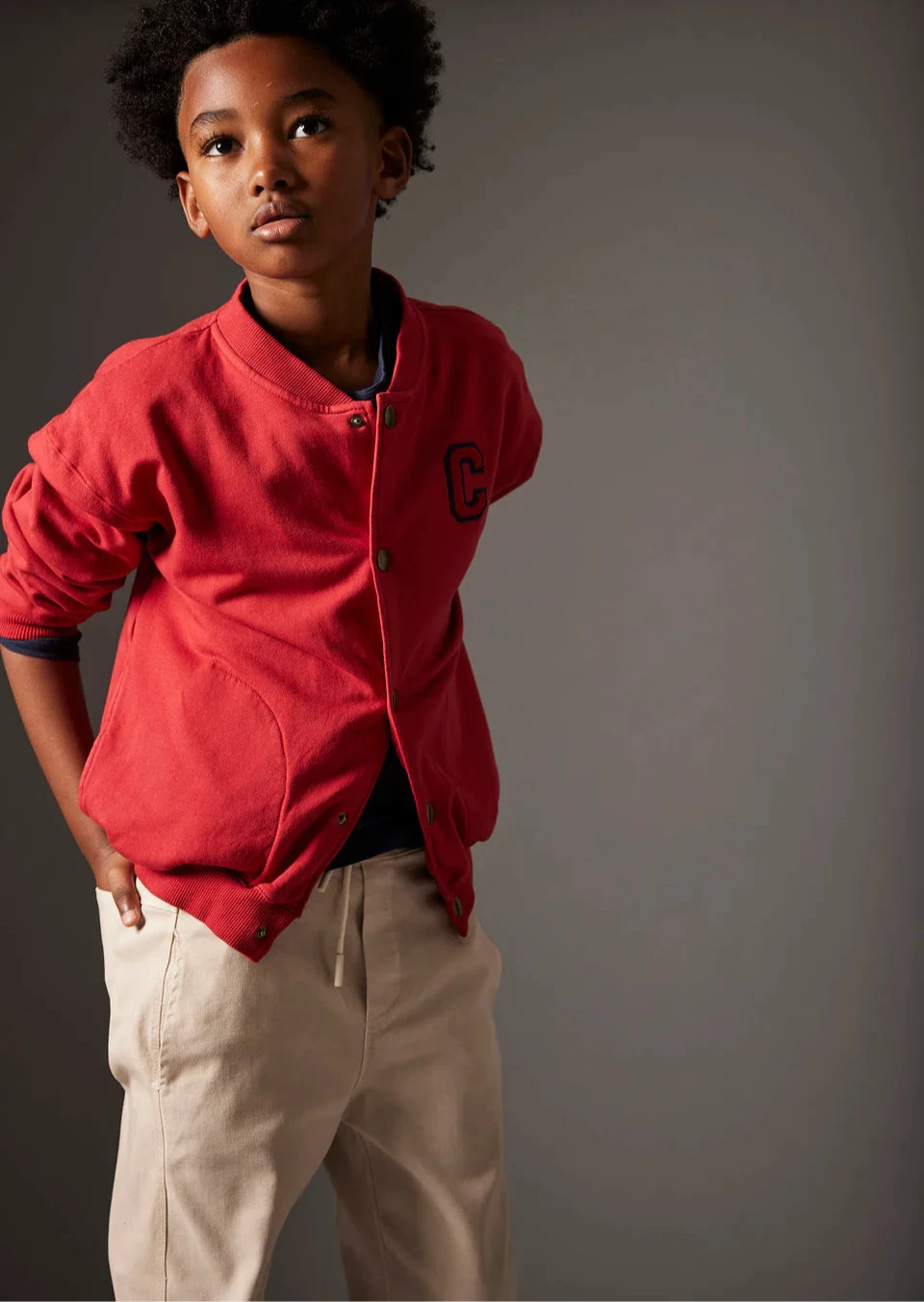 Child wearing a red jacket and khaki pants on a plain background