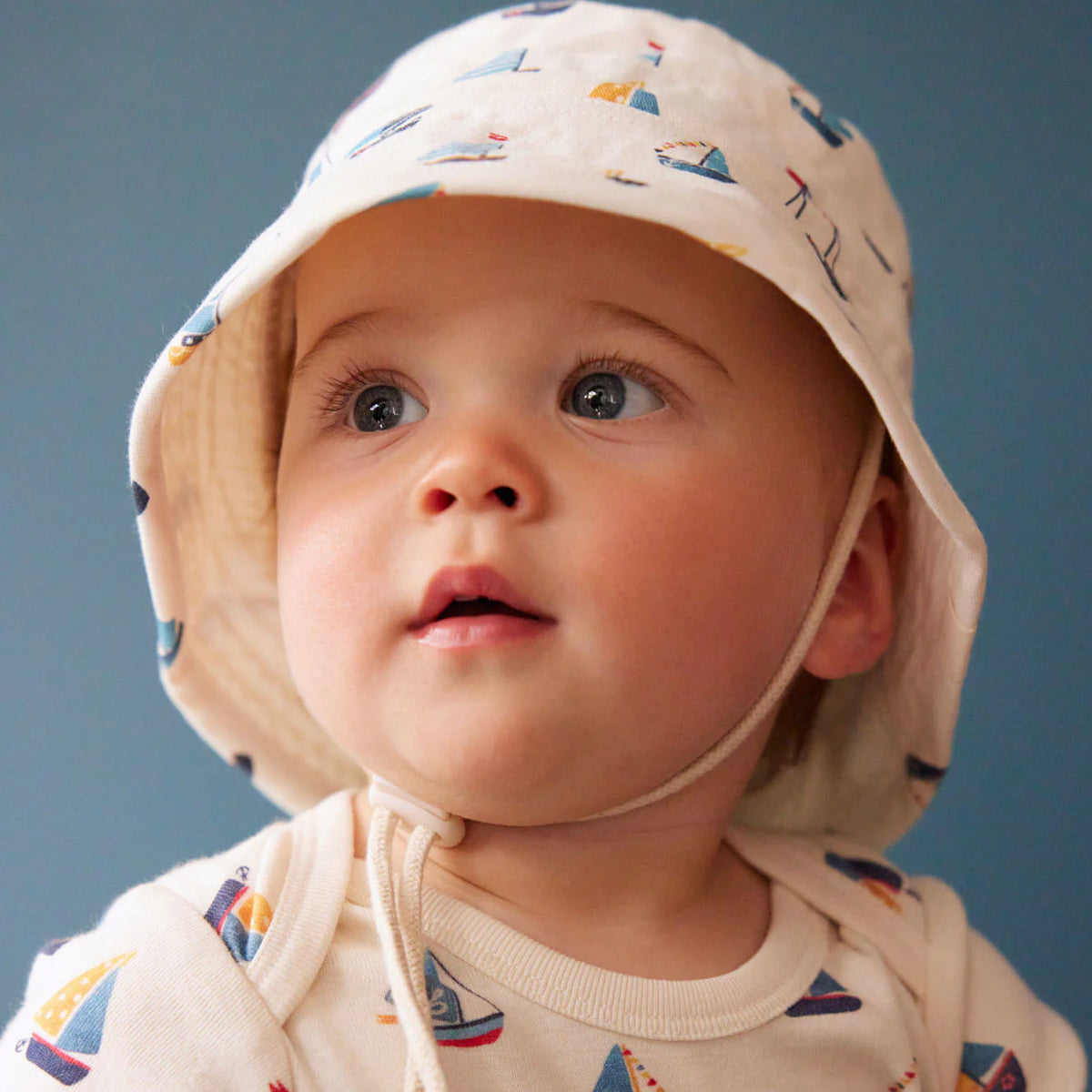 Baby wearing a patterned hat and shirt against a blue background