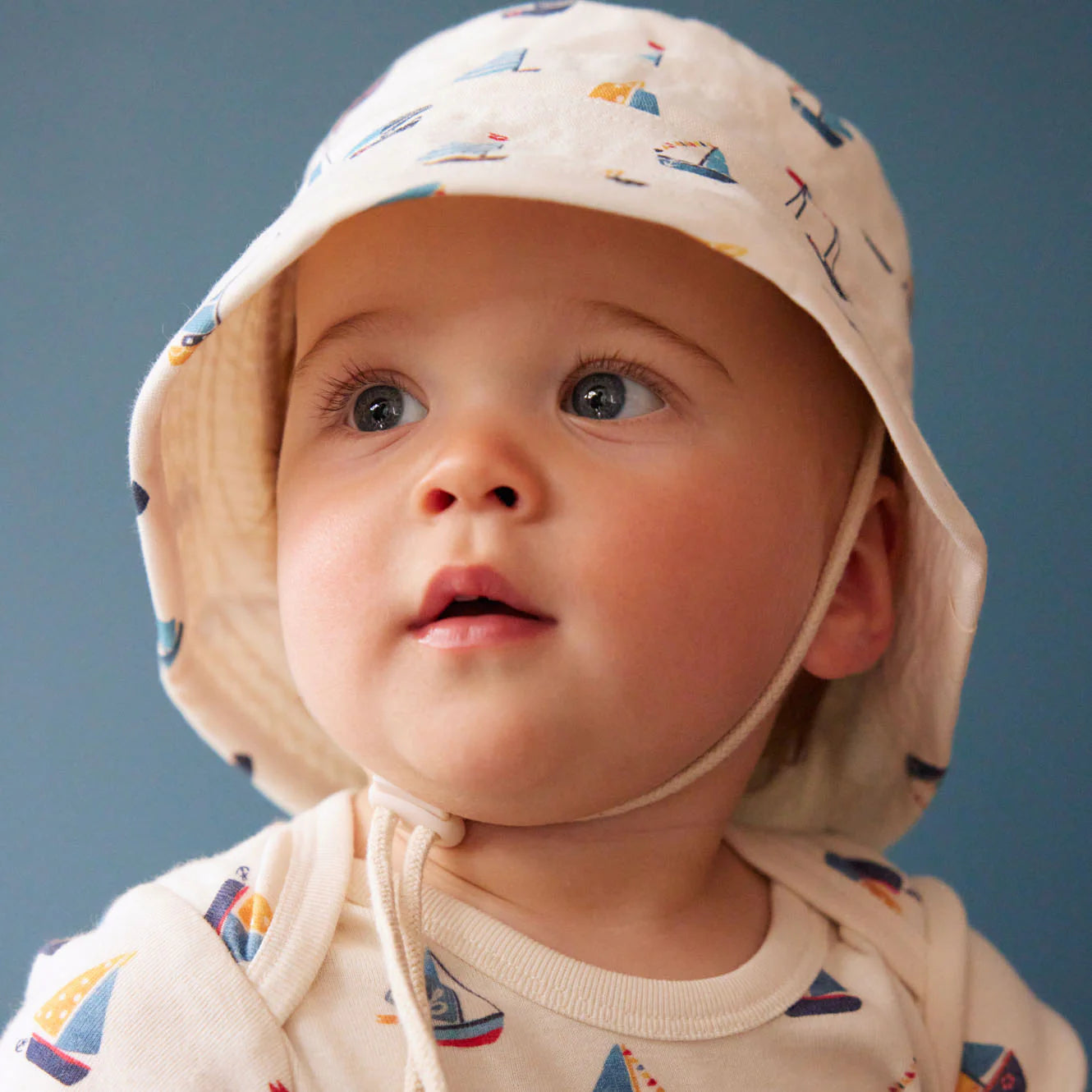 Baby wearing a patterned hat and shirt against a blue background