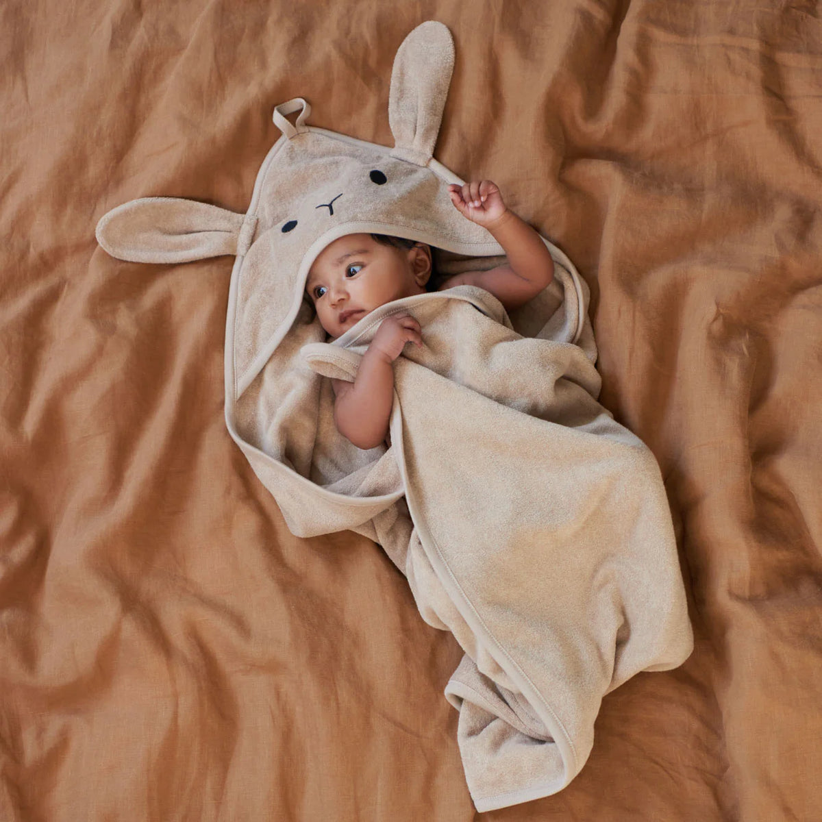 Baby wrapped in a beige bunny hooded towel on a brown blanket
