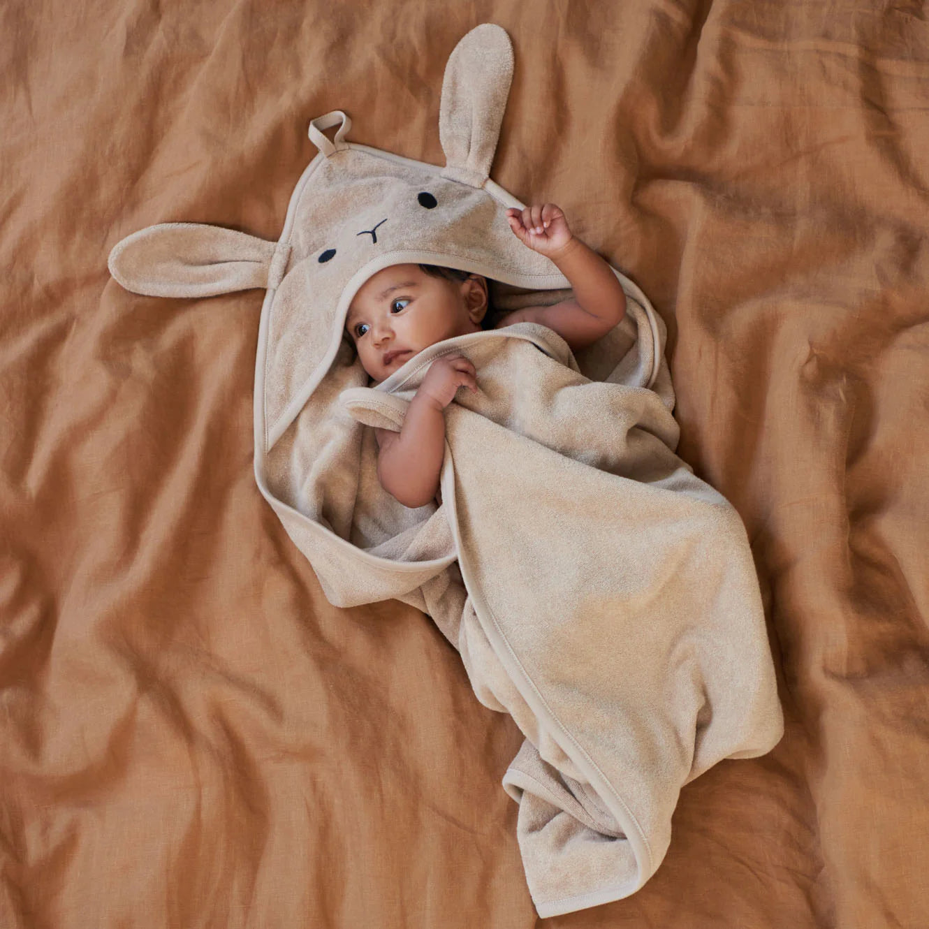 Baby wrapped in a beige bunny hooded towel on a brown blanket